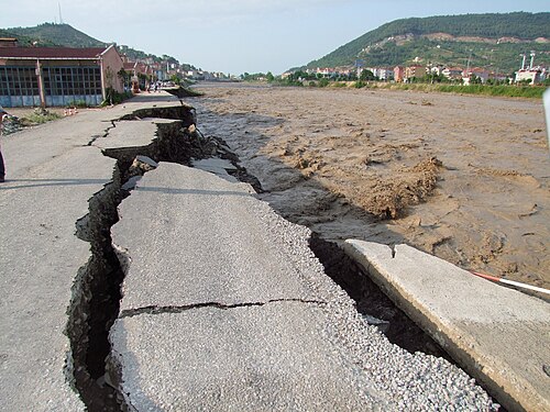 大きな亀裂のある道路が、激しく濁った茶色の川によって洗い流されている。