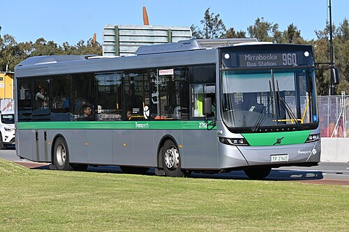 薄緑、オレンジ、白のバスが、高層ビルの前で停車している。