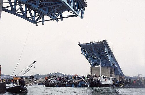 聖水大橋の下の漢江から見た、橋の失われた部分。曇り空で、橋の端には小さな群衆が集まっている。橋の崩落部分には、クレーンを含め、多くの船や人々が群がっている。