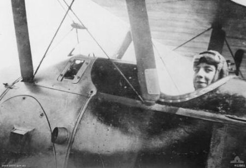 飛行機の側面のクローズアップ写真。帽子をかぶり、額にゴーグルをつけた男性がコックピットに座っている。