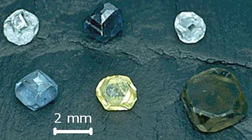 立方八面体の結晶が 6 つあり、それぞれ直径が約 2 ミリメートルです。2 つは淡い青、1 つは淡い黄色、1 つは緑がかった青、1 つは濃い青、1 つは緑がかった黄色です。