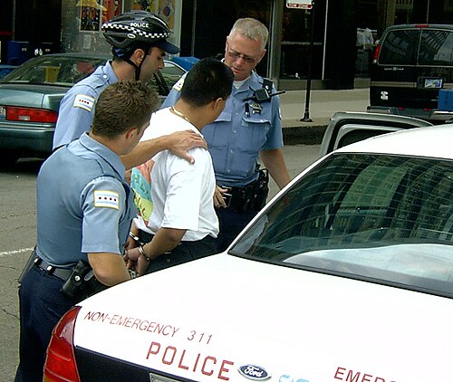 3人の警察官が、手錠をかけられたTシャツ姿の男を取り囲んでいる。