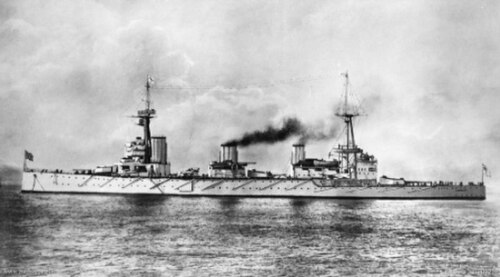 3 本の煙突と 2 本の大きなマストを備えた大型軍艦の側面図。船は静止しており、中央と後部の煙突から煙が出ています。