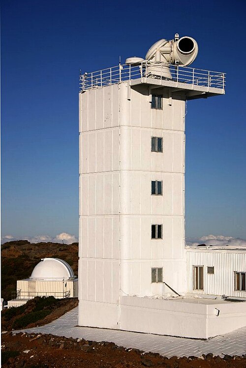 大きな望遠鏡を備えた柵で囲まれたバルコニーを備えた 6 階建ての建物の写真