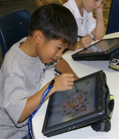 灰色のTシャツを着たアジア人の少年が丸いテーブルでタブレットコンピューターを使っている