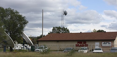 近くの高速道路から見える、赤い Fox 25 WLAX - TV の看板と、その隣にあるアンテナ付きの小さな塔がある、茶色の小屋のような建物。