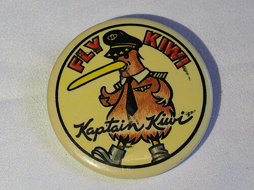 1994 年頃の Kiwi International Airlines のプロモーション ボタン。直径 54 mm。背景は黄色で、航空会社の機長帽、ネクタイ、翼、肩章を身に着けた Kiwi 鳥の漫画の図が描かれています。上部に赤いブロック体で「FLY WIKI」、下部にスクリプトで「Kaptain Kiwi」と書かれています。