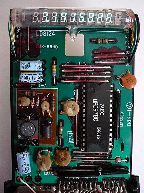 1970年代半ばに製造されたカシオの関数電卓fx-20の内部構造。VFD（可変周波数ドライブ）を使用している。プロセッサICはNEC製（μPD978Cと表記）。コンデンサや抵抗などの個別電子部品とICはプリント基板（PCB）上に実装されている。この電卓はバッテリーパックを電源として使用している。