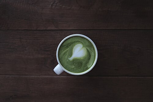 抹茶が入った白いマグカップに、ラテアートでハートが描かれている様子を上から見た写真。
