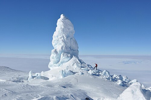 氷に覆われた風景の中に、中央に巨大な氷の塔があり、大きさを比較するために人間が写っている写真。