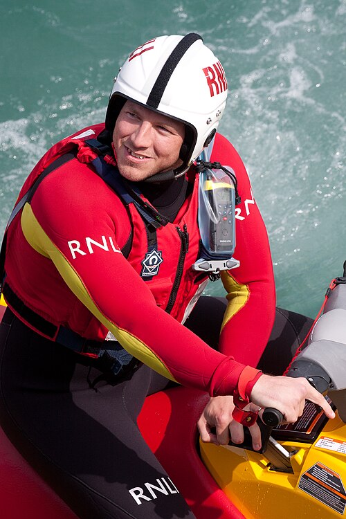 RNLI の乗組員がヘルメットと真っ赤なウェットスーツを着て、小さなインフレータブルに座っている。