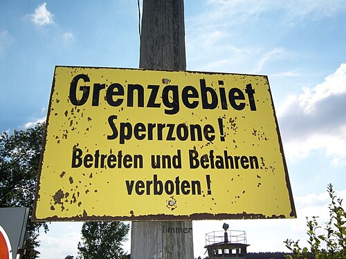 ポールに取り付けられた黄色の看板には、「Grenzgebiet Sperrzone! Betreten und befehren verboten!」と書かれています。