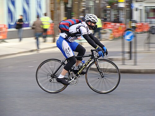 スポーツウェアを着て白いヘルメットをかぶった男性が道路で自転車に乗っています。