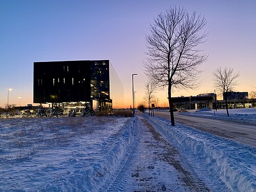 夕日を背景にした黒い建物のファサード。夕日が建物の側面に反射しています。地面は雪に覆われています。