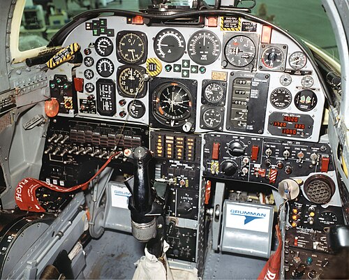 多数の古い円形のダイヤルとゲージを備えた航空機のコックピット。コントロールの前には黒いスティックの操縦桿があります。