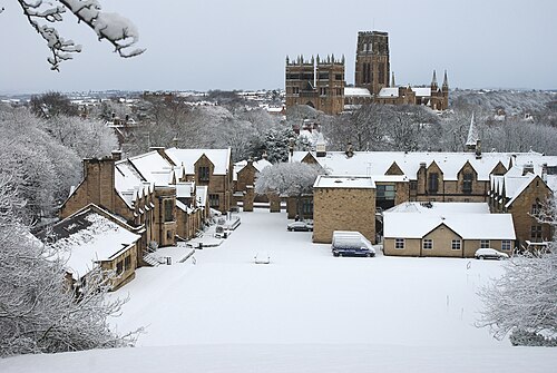 雪景色の中のダラム・スクール礼拝堂と、背景に写るダラム大聖堂の写真