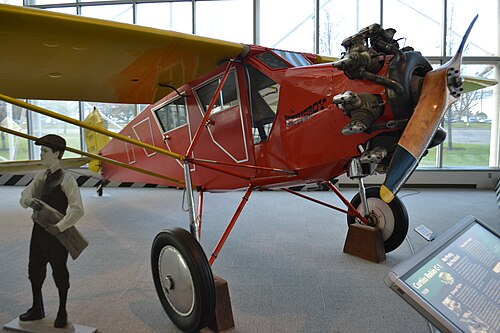 上部に単翼の小型飛行機。前方に木製プロペラ 1 個。胴体には「Newsboy」の文字が描かれている。