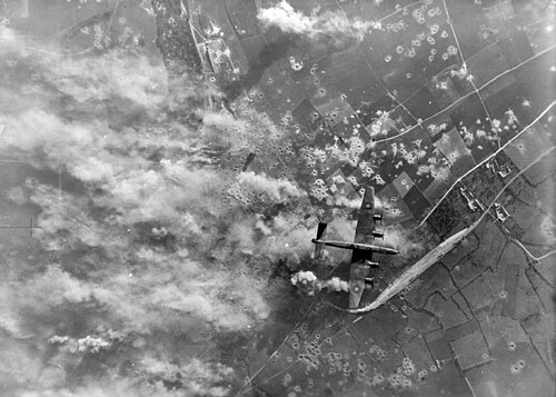 イギリスの爆撃機が、多数のクレーターと煙の柱が真下に見えている、激しく爆撃された農地の上空を飛行している。