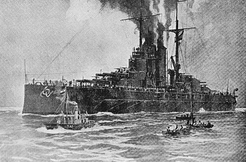 大きな戦艦が煙突から煙を出し、水中で動かずに停泊しており、前景では 3 隻の小型ボートが戦艦の横を移動しています。