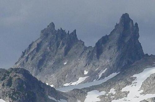 背景の周囲の地形よりも高くそびえる、急峻な垂直の岩山を背景にした、軽く氷河に覆われた山岳風景。