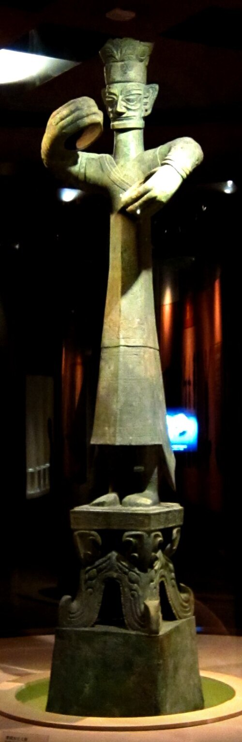 王でありシャーマンの指導者でもある人物の立像。紀元前1200年～1000年頃。おそらく青銅製。全高：2.62メートル。三星堆博物館（中国四川省広漢市）