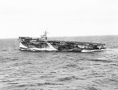 海上の航空母艦の白黒写真。船尾は船首よりも水中にかなり低くなっています。