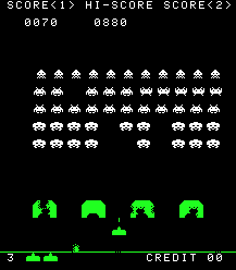 縦長の長方形のビデオゲームのスクリーンショット。エイリアンとレーザー砲の戦いをデジタルで表現した画像である。白いエイリアンが、4つの緑色の逆U字型のブロックの上に浮かんでいる。ブロックの下には、上部に三角形が付いた小さな横長のブロックがある。