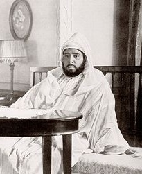 テーブルの後ろの長椅子に座るスルタン・アブデルハフィド