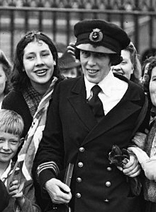 MBE を受賞したビクトリア・ドラモンドの白黒写真。彼女は海軍の制服を着て、女性と子供たちに囲まれています。