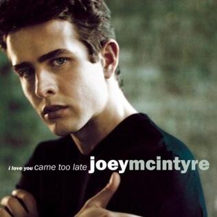 ジョーイ・M は黒い T シャツを着て、両手を肩に組んで、暗い表情を浮かべています。