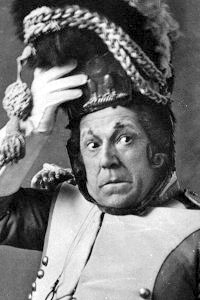 1840年代のフランス軍の軍服を着た中年の白人男性の頭と肩の写真。片手で扱いにくい帽子を押さえ、滑稽なほど不安そうな顔をしている。