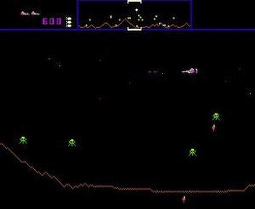 惑星の表面をデジタルで表現した、横長の長方形のビデオ ゲームのスクリーンショットです。右上隅にある白い三角形の宇宙船が、緑色のエイリアンの敵と戦っています。画面の上部には、アイコン、数字、および地形のミニチュア バージョンを表示するバナーがあります。