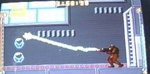 パワード外骨格を装着した人物がビームを発射するビデオゲームのスクリーンショット。