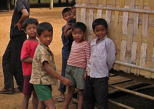 編み壁のある建物の前に立つ6人の幼い子供たち